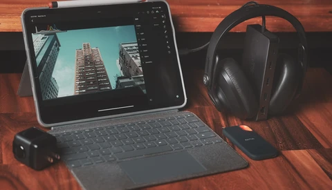 Tablet displaying architectural photography with editing software open, surrounded by headphones and external hard drive on wooden surface.