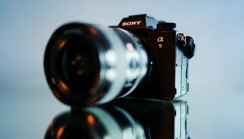 Sony α9 mirrorless camera with telephoto lens mounted, photographed against a neutral sky background with reflective surface below.