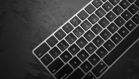 Overhead view of a silver and black wireless keyboard on a dark textured surface.