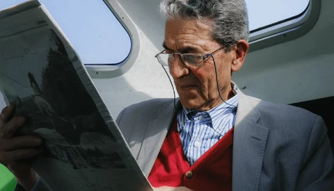 Man in blazer and red cardigan reviewing tablet outdoors near aircraft.