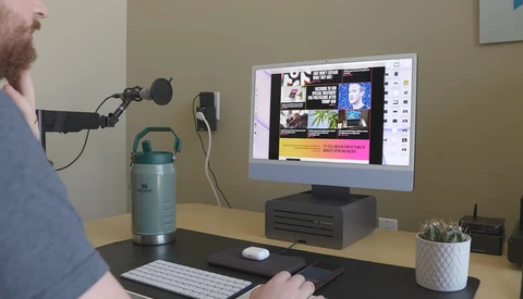 Podcaster or content creator speaking into a microphone at a desk setup with monitor displaying editing software.