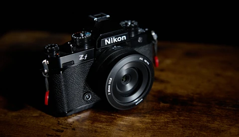 Nikon Zf mirrorless camera with attached lens on wooden surface against dark background.