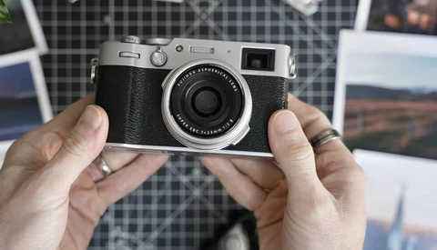 Hands holding a silver and black rangefinder camera with fixed lens against a plaid background.