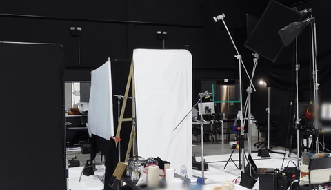 Professional photography studio setup with large white reflector panel, multiple light stands, and softbox lighting on black walls.
