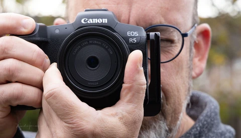 Man holding a Canon EOS R5 mirrorless camera with an RF 35mm lens attached.