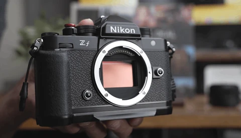 Nikon Z5 mirrorless camera body held in hands, showing the front mount and control layout against a blurred interior background.