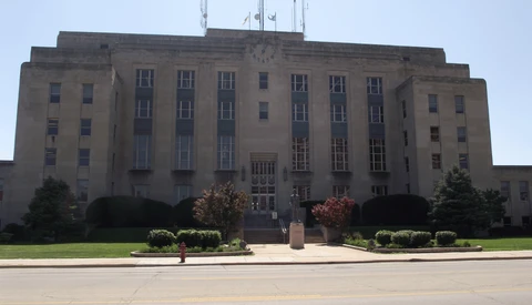 Symmetrical Art Deco government building with tan stone facade, central clock tower, and manicured landscaping.