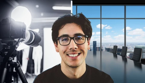 Man wearing glasses smiling at camera in modern office with professional lighting setup visible.