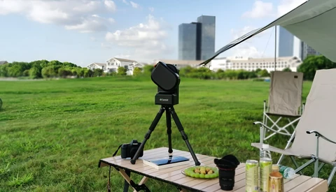 Camera mounted on tripod at outdoor picnic setup with city skyline in background.