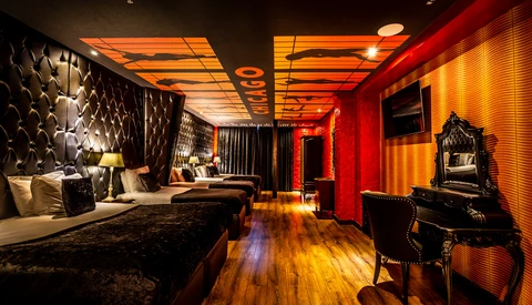 Luxury hotel bedroom with dramatic red and gold lighting, quilted headboard, and ornate mirror at vanity.