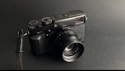 Black rangefinder camera with leather strap on dark gray background.