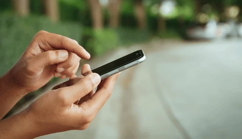 Hands holding a smartphone outdoors with blurred garden background.