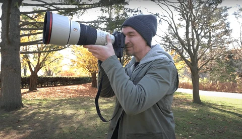 Photographer holding a telephoto lens camera in an outdoor park setting during golden hour.