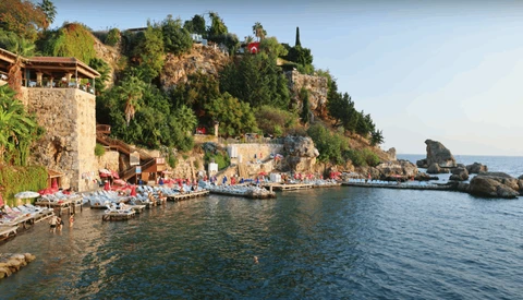Mediterranean coastal settlement with stone buildings built into a hillside overlooking a calm bay with boats.