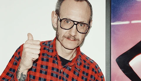 Man with glasses and mustache wearing red plaid shirt giving thumbs up gesture.