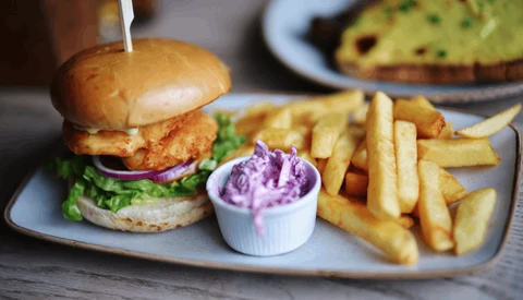 Crispy fried chicken sandwich with purple onions, lettuce, and golden fries served with purple aioli sauce.