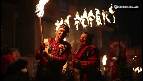 Two people in red ceremonial robes holding flaming torches during a nighttime procession.