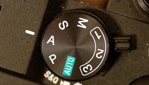 Close-up of a camera mode dial showing P, A, S, M, and AUTO settings with the dial positioned on AUTO.