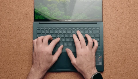 Overhead view of hands typing on a laptop keyboard with a nature scene displayed on the screen.