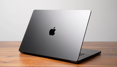 Space gray MacBook Pro closed on wooden surface against neutral background.
