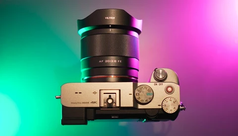 Mirrorless camera with wide-angle zoom lens mounted, displayed against gradient cyan and magenta lighting.
