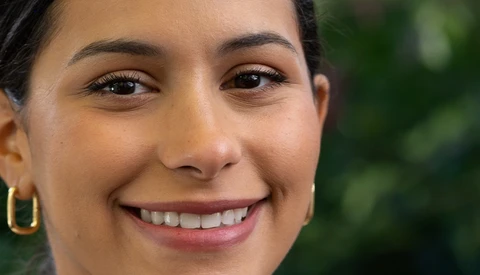 Close-up portrait of a woman smiling at the camera with natural outdoor lighting.
