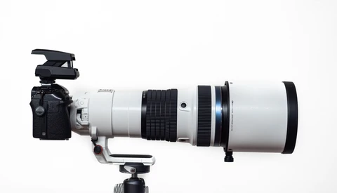 Professional telephoto lens with white barrel mounted on camera body with tripod collar and microphone attachment.