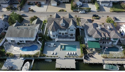 Aerial view of waterfront homes with pools and docks along a residential canal.