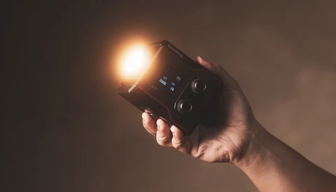 Hand holding a compact flashlight with bright warm LED beam against dark background.
