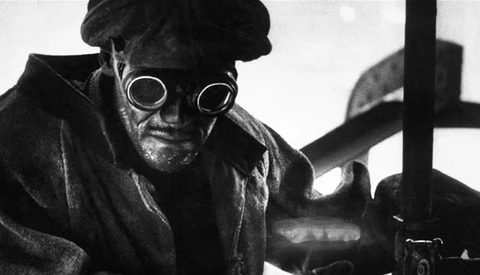 Black and white portrait of a person wearing circular goggles and dark clothing, shot from a low angle.