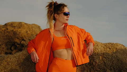 Woman in bright orange athletic wear posing against large boulders in natural daylight.