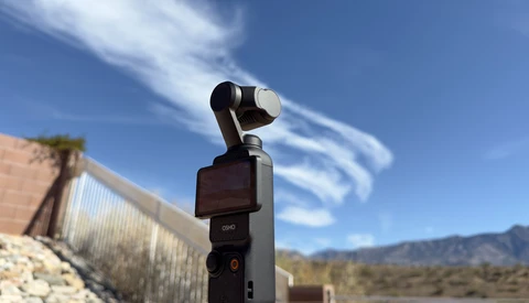 DJI Osmo Pocket gimbal camera mounted on a fence post overlooking desert landscape under blue sky.