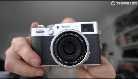 Hands holding a rangefinder camera with chrome top plate and black leather body.