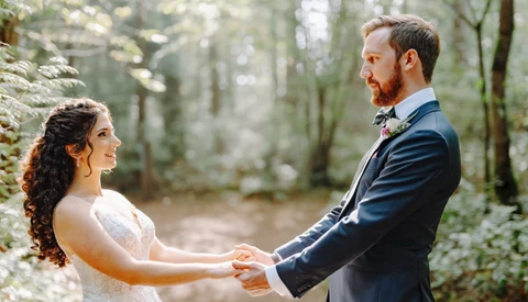 Bride and groom holding hands facing each other in a forest setting.