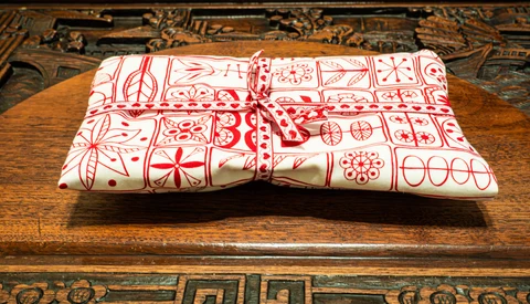 Red and white patterned fabric gift wrapped with twine bow on wooden table with ornate carved border.
