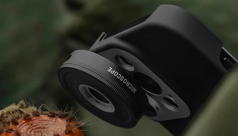 Close-up of a black telephoto lens converter or attachment mounted on camera equipment against blurred green background.