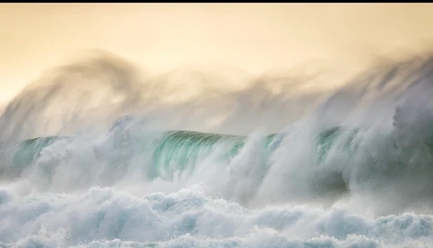 Powerful ocean waves with turquoise-green water and white foam crashing in sequence.