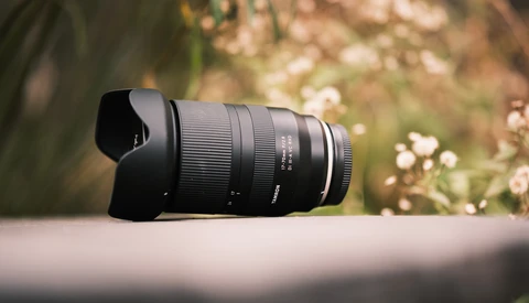 Black telephoto lens with hood mounted on neutral surface against blurred garden background.