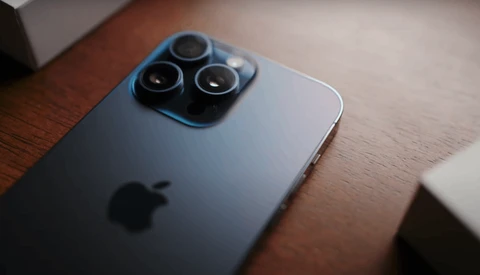 iPhone with triple-lens camera module photographed at an angle on a wooden surface.