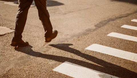 Person's legs and shadow crossing a zebra crossing on pavement in bright sunlight.