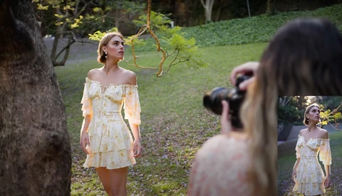 Woman in cream off-shoulder dress standing in garden during outdoor portrait shoot.
