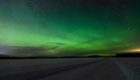 Aurora borealis illuminates the night sky in brilliant green above a frozen landscape and dirt road.