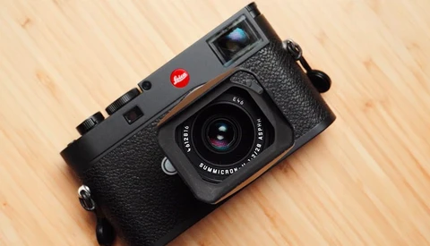 Leica M6 rangefinder camera with black leather strap on wooden surface.