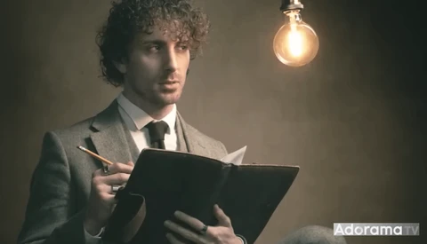 Man in business suit holding tablet with pencil under warm incandescent bulb.