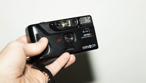 Hand holding a Minolta AF point-and-shoot camera with built-in flash and viewfinder.