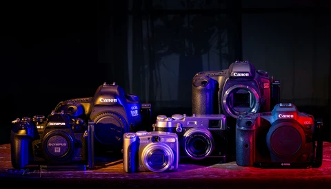 Collection of Canon and Olympus digital cameras illuminated with blue and red LED lighting against a dark background.