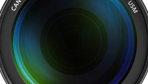 Close-up view of a camera lens barrel showing multicoated glass elements with blue and green light reflections.