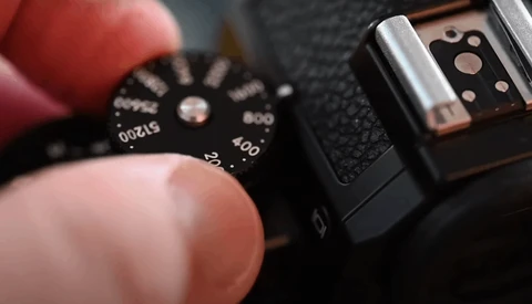 Close-up of a camera's ISO dial being adjusted by a photographer's finger.