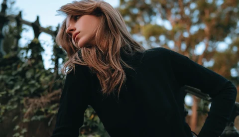 Woman in black long-sleeve top looking over shoulder outdoors during golden hour.