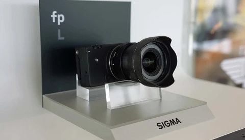 Sigma lens mounted on fp L camera body displayed on white pedestal with branding.